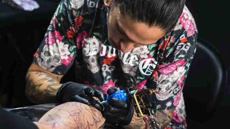 Tattoo artist focused on designing a detailed tattoo on a client's arm in a studio setting., tags: van - pexel