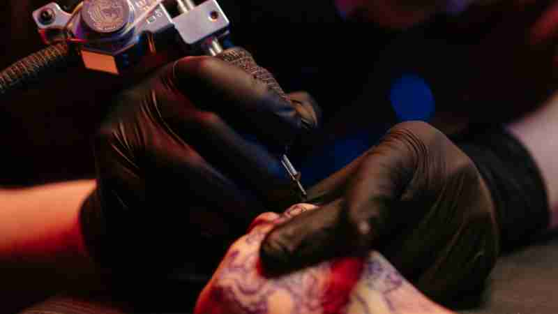Close-up of a tattoo artist in gloves skillfully tattooing intricate design on a forearm., tags: tatoeëerder voor zwart-grijze - pexel