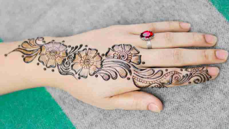 Close-up of hand with floral henna mehndi design and ruby ring on a green and gray background., tags: zich op van - pexel